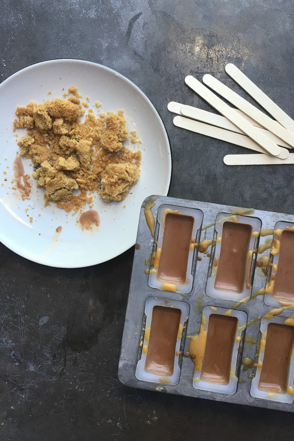 Chocolate Peanut Butter Popsicles made with chunks of peanut butter cookie, peanut butter cups and a drizzle of peanut butter in each popsicle! Find the recipe on Shutterbean.com